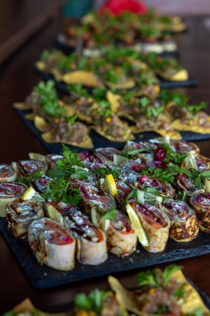 Assorted gourmet appetizers presented on dark platters, garnished with fresh herbs and lemon slices.