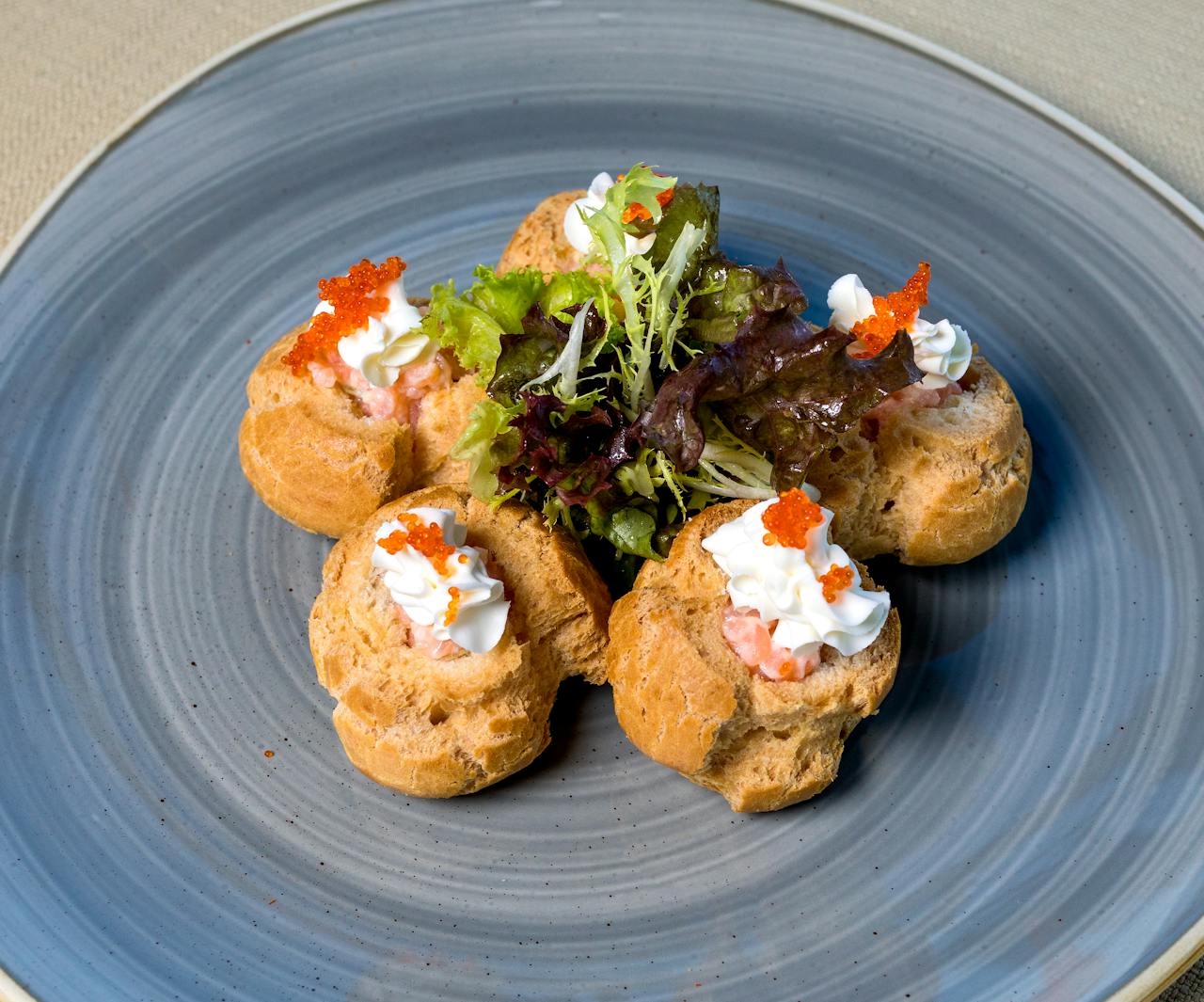 Elegant puff pastries topped with caviar and cream cheese, garnished with fresh greens.
